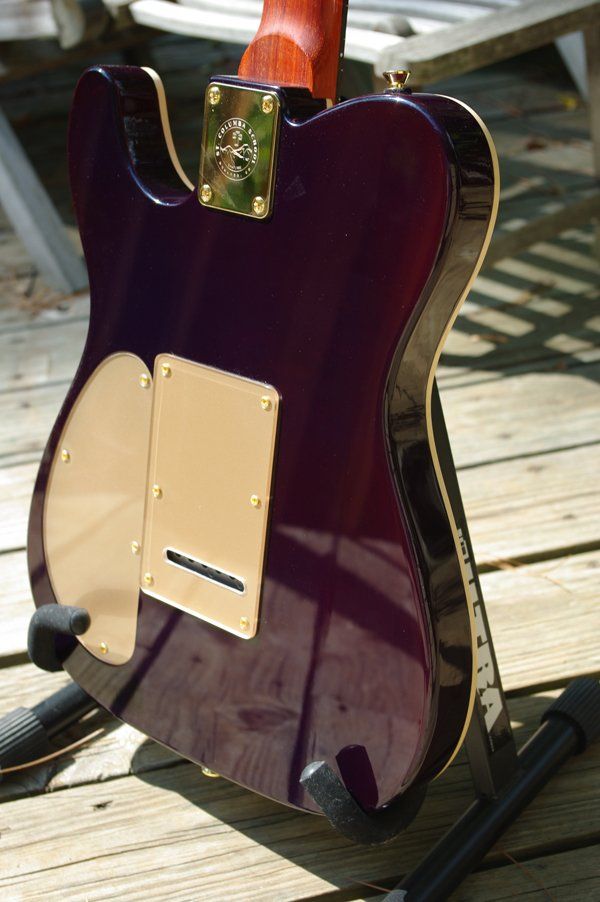 A purple electric guitar is sitting on a wooden deck