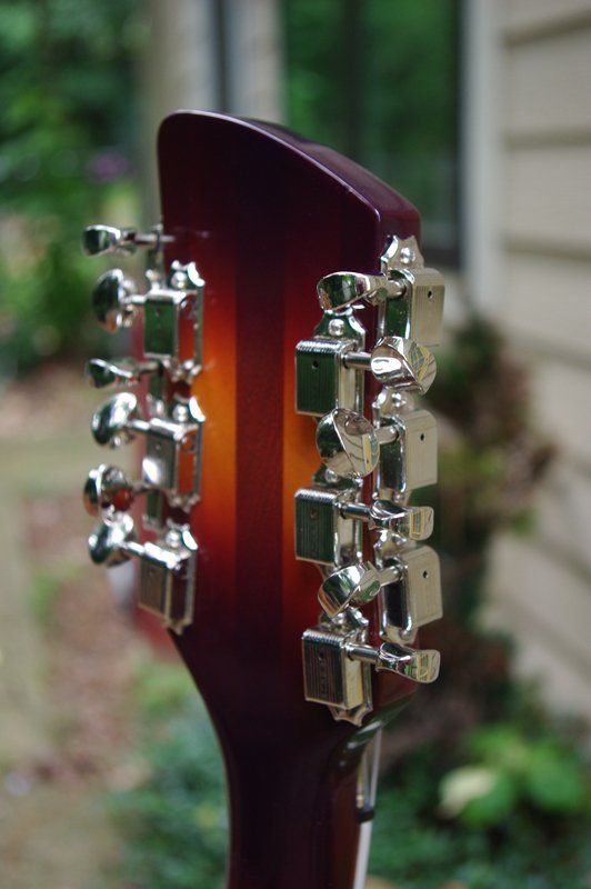 A close up of a guitar headstock with a house in the background