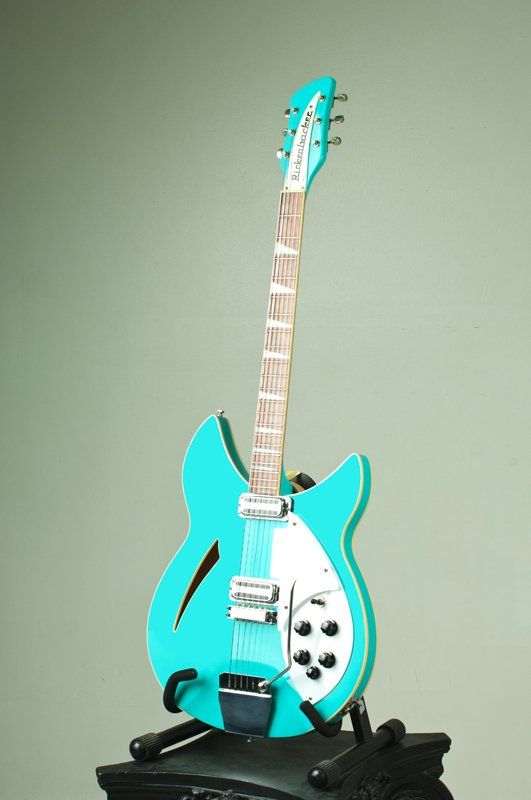 A turquoise electric guitar is sitting on top of a black stand.