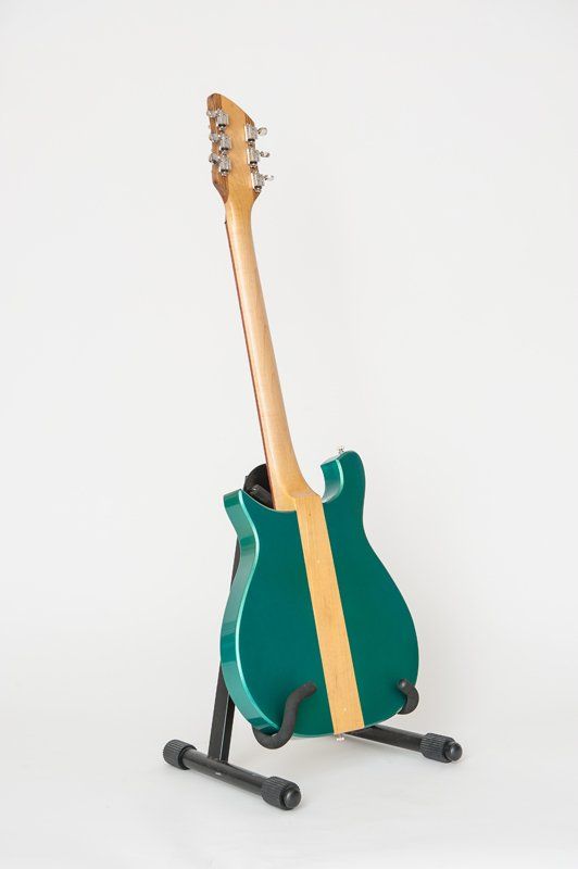 A green guitar is sitting on a black stand on a white background.