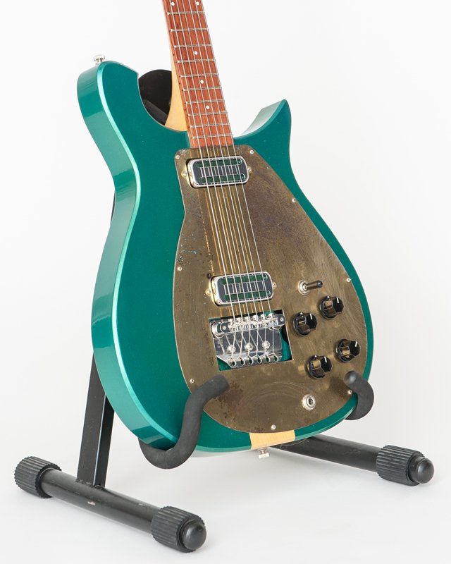 A green guitar is sitting on a black stand