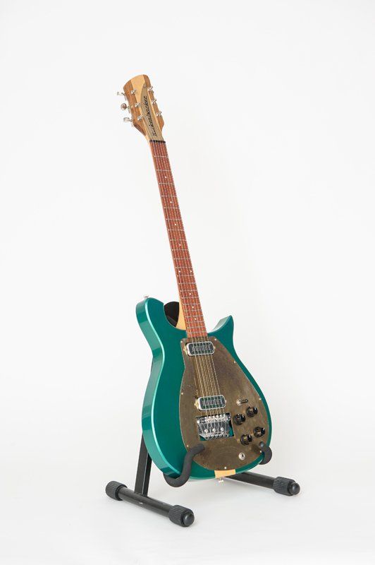 A green electric guitar is sitting on a stand on a white background.