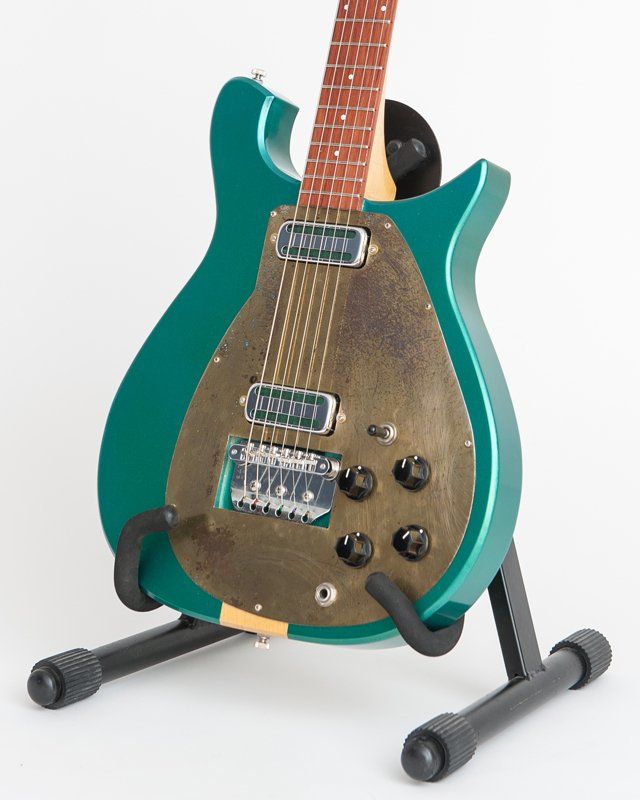 A green guitar is sitting on a black stand