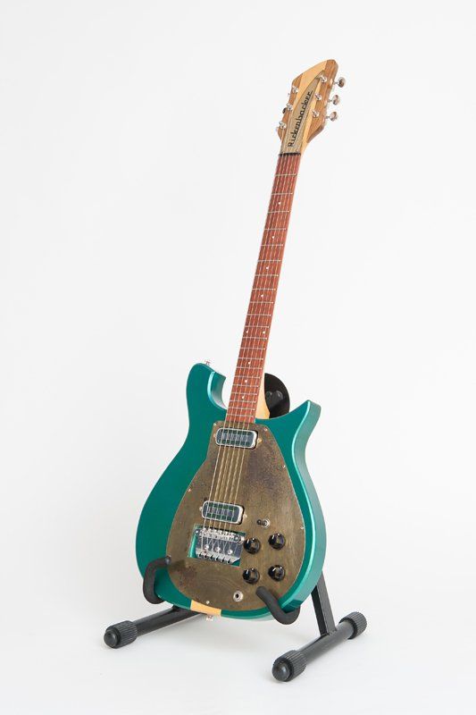 A green electric guitar is sitting on a stand on a white background.