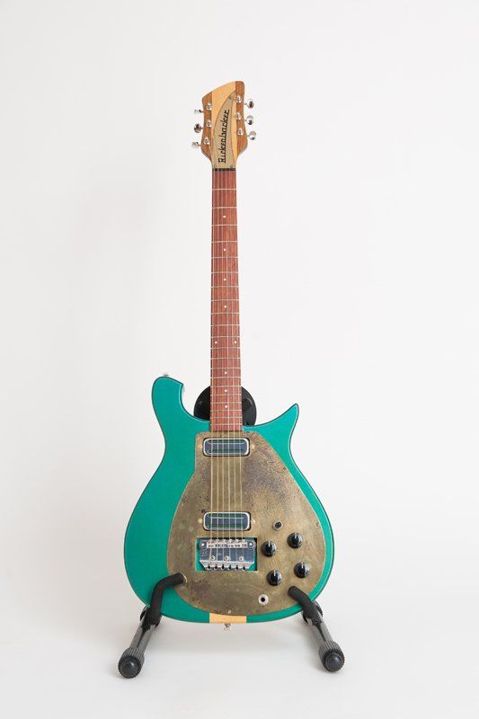 A green electric guitar is sitting on a stand on a white background.
