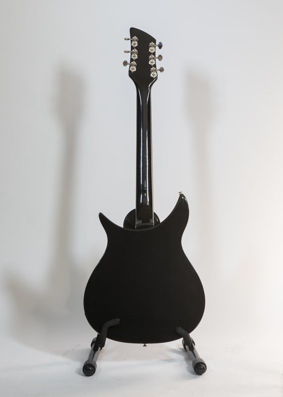 A black electric guitar is sitting on a stand on a white background.