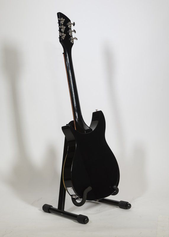 A black electric guitar is sitting on a stand
