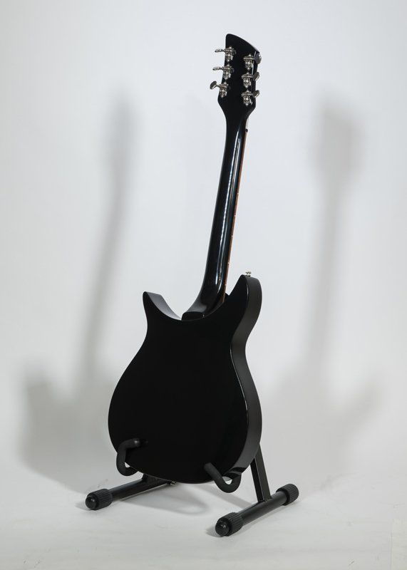 A black electric guitar is sitting on a stand