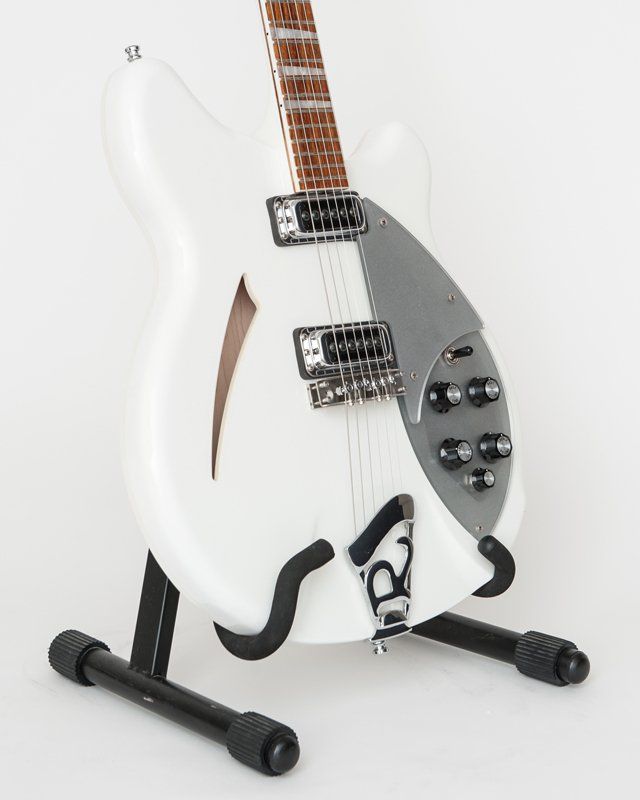 A white guitar is sitting on a black stand