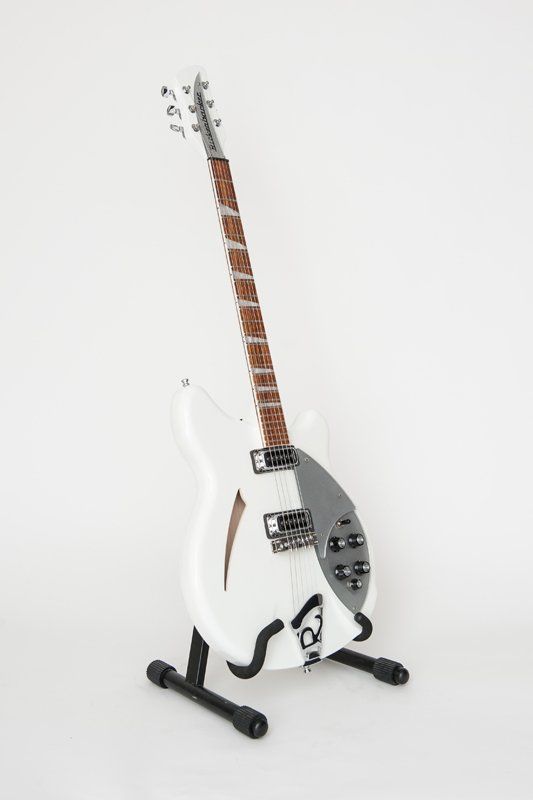 A white guitar is sitting on top of a black stand.