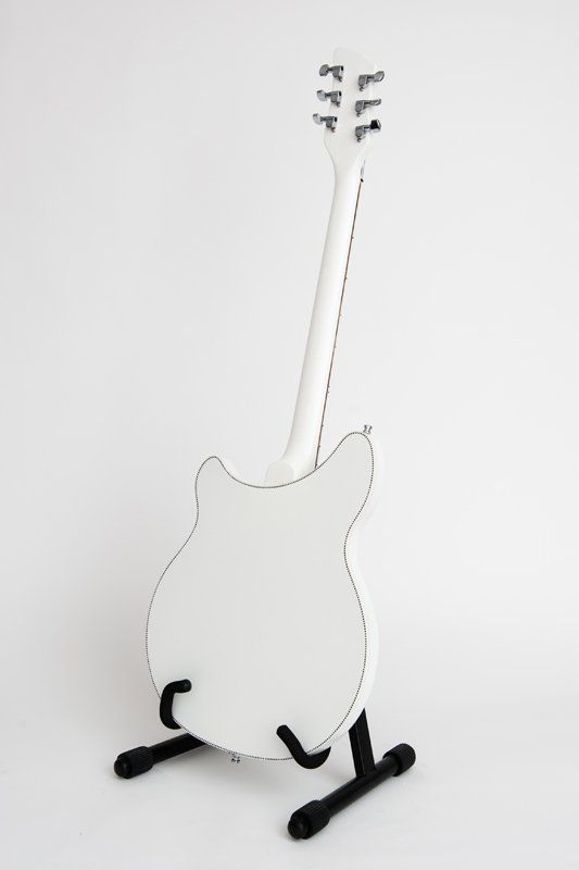 A white guitar is sitting on a black stand.