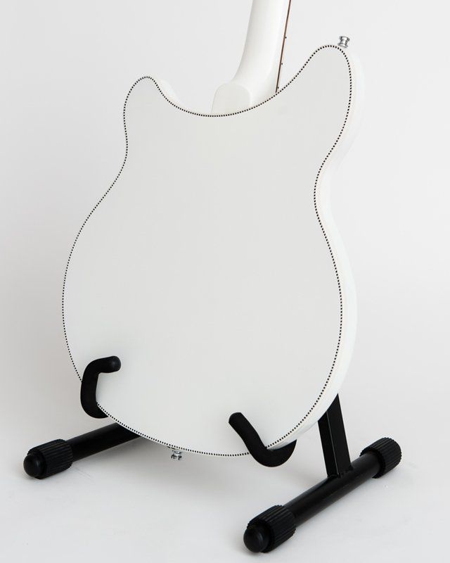 A white guitar is sitting on a black stand