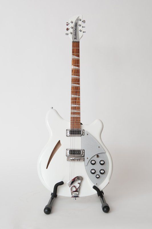 A white rickenbacker guitar is sitting on a stand