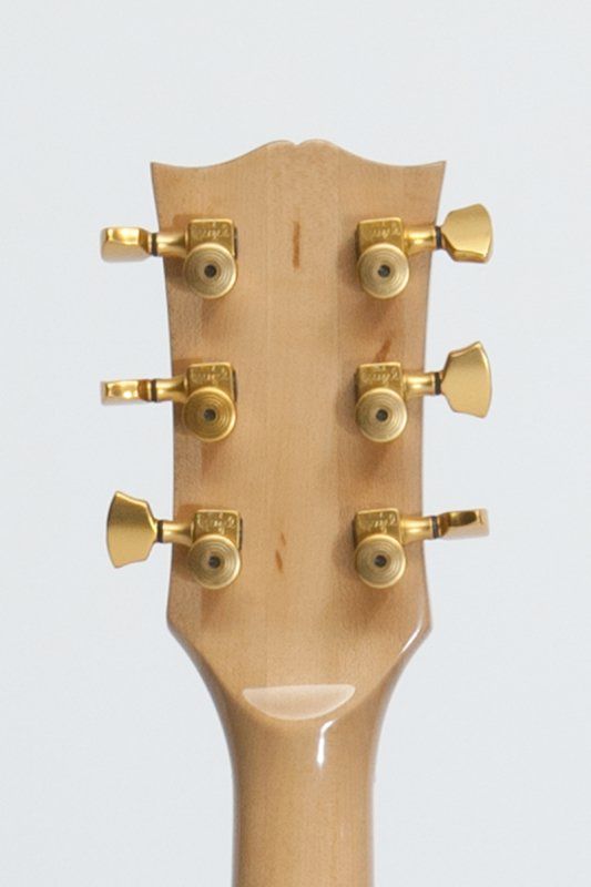 A close up of a guitar headstock with gold knobs