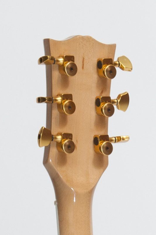 A close up of a guitar headstock with gold knobs