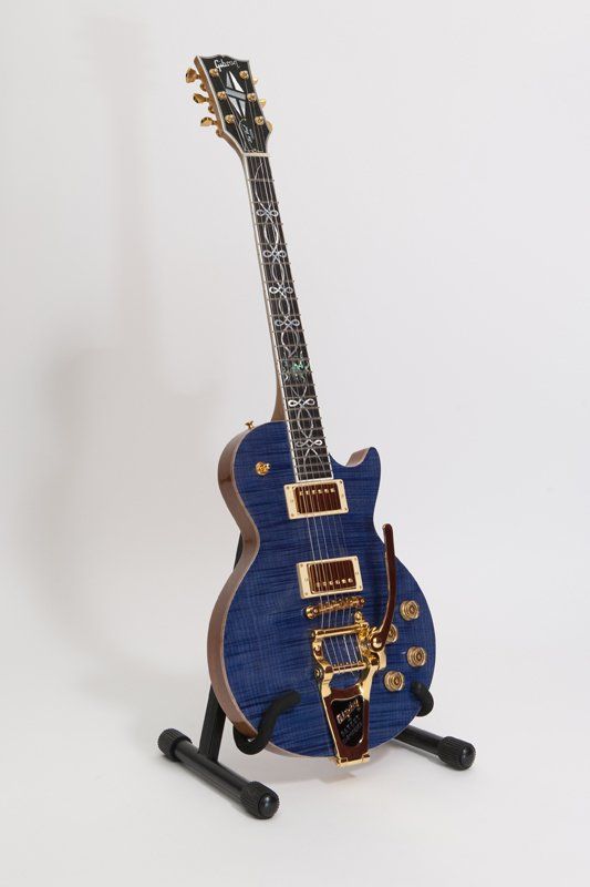 A blue electric guitar is sitting on a stand on a white background.