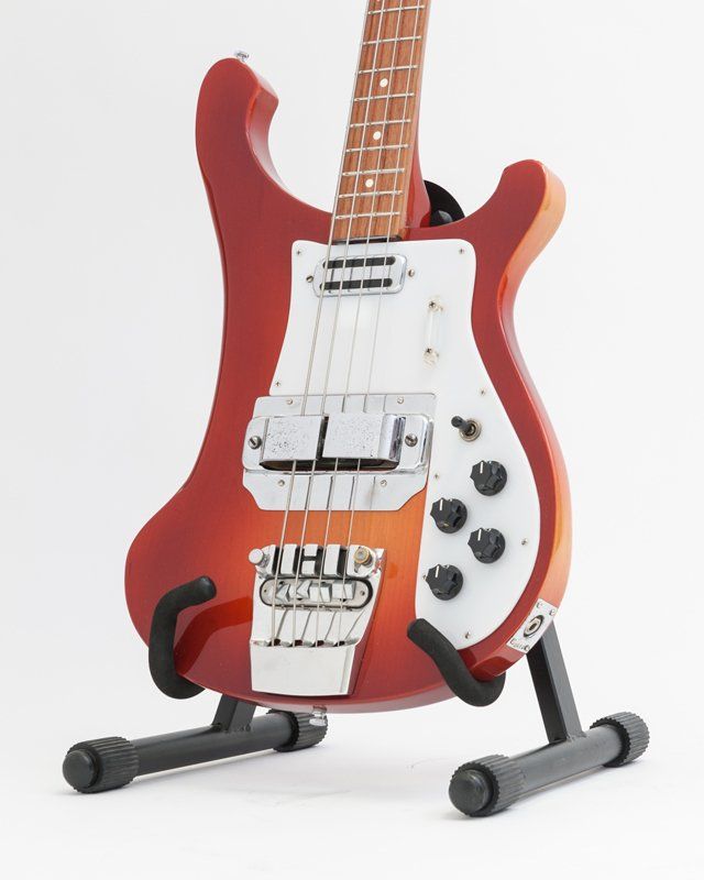 A red and white bass guitar is sitting on a stand