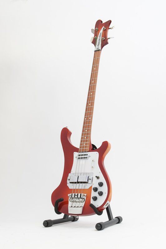 A red electric guitar is sitting on a stand on a white background.