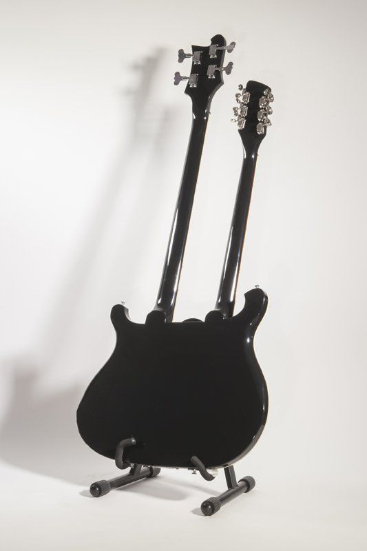 A black double neck guitar is sitting on a stand