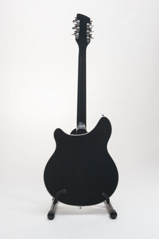 A black electric guitar is sitting on a stand on a white background.