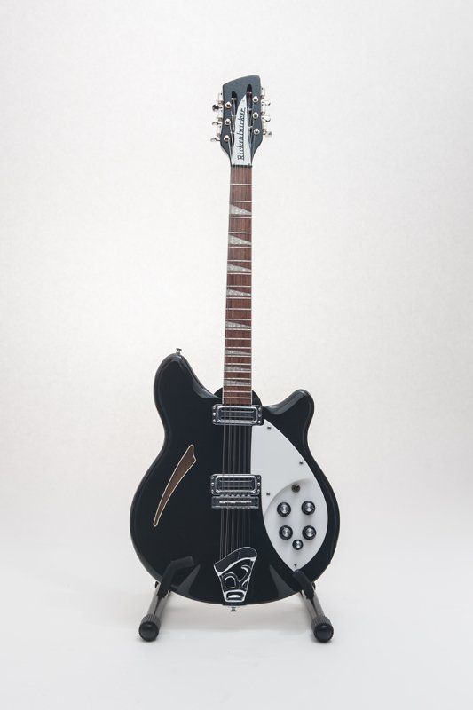 A black electric guitar is sitting on a stand on a white background.