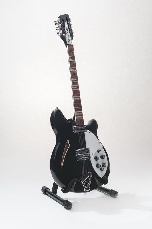 A black guitar is sitting on a stand on a white background.