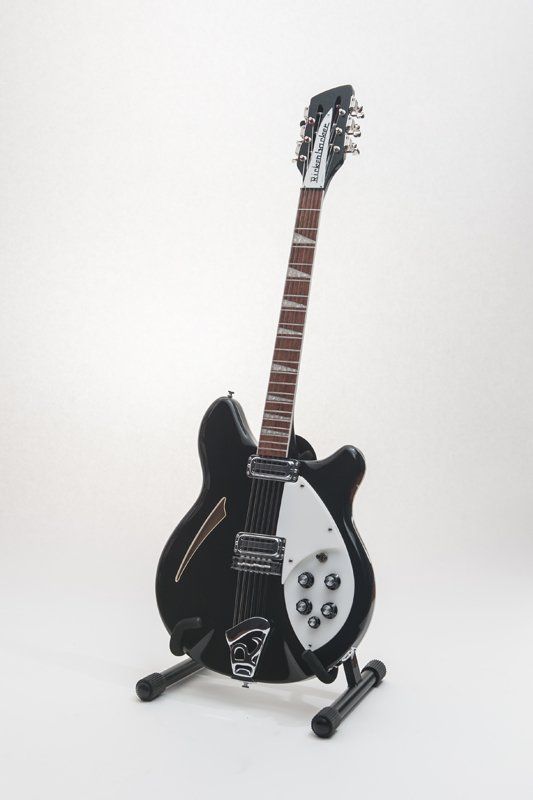 A black electric guitar is sitting on a stand on a white background.