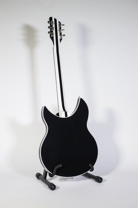 A black and white electric guitar is sitting on a stand.