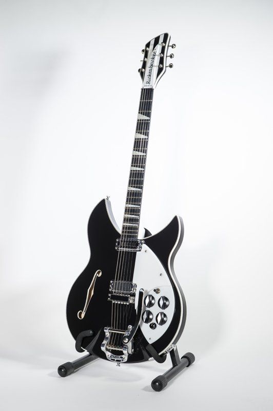 A black electric guitar is sitting on a stand on a white background.