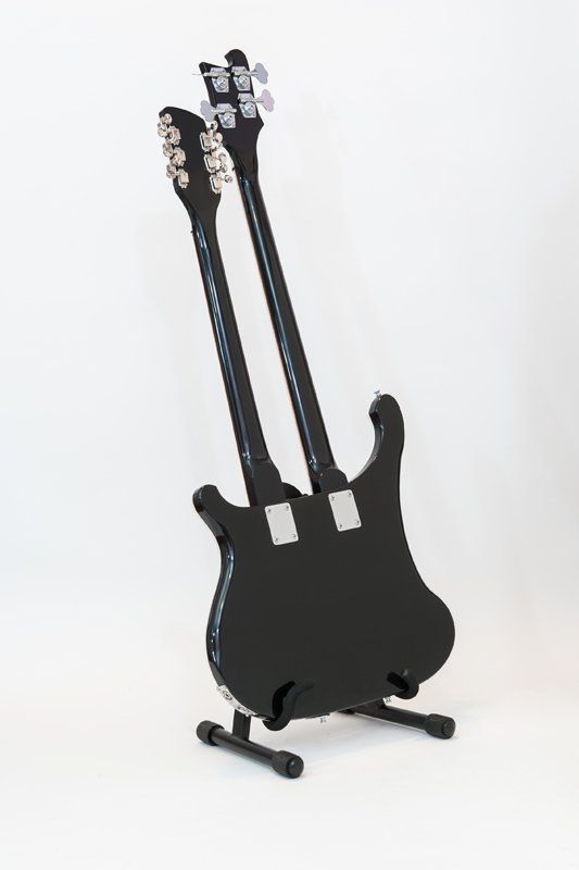 A black double neck guitar is sitting on a stand.