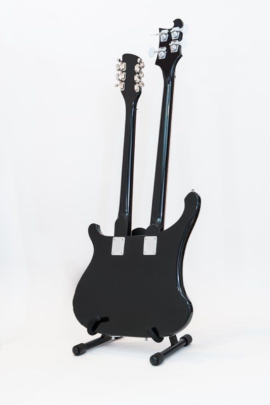 A black double neck electric guitar is sitting on a stand.