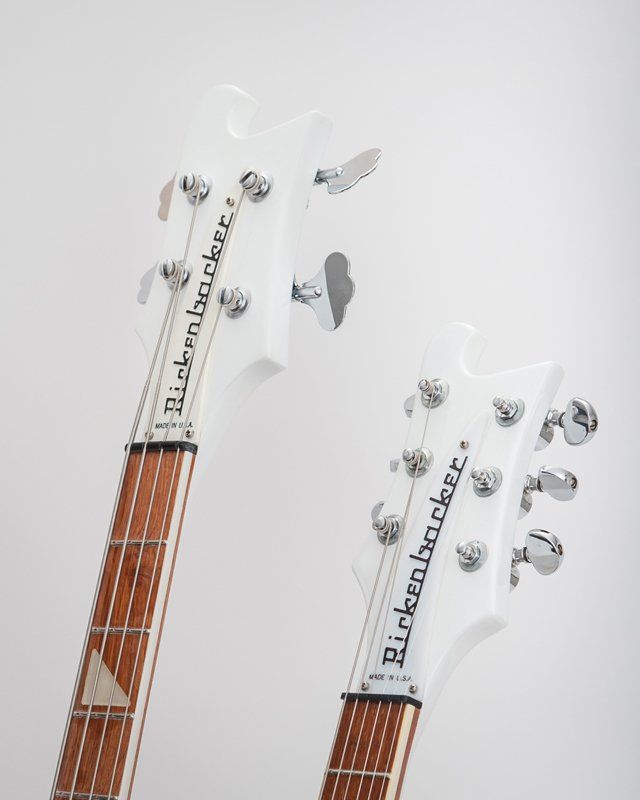 Two white rickenbacker guitars are sitting next to each other on a white surface.