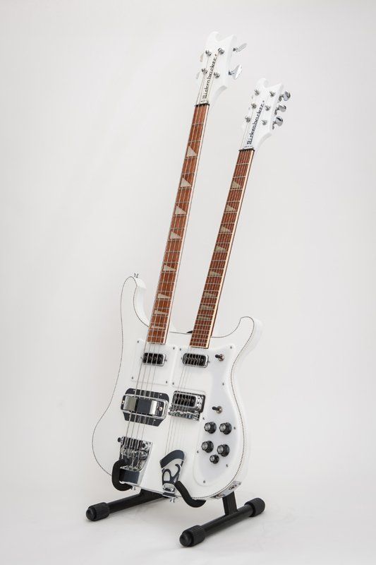 A white double neck electric guitar is sitting on a stand.