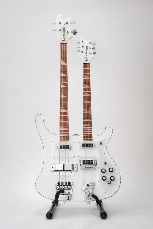 A white double neck electric guitar is sitting on a stand.