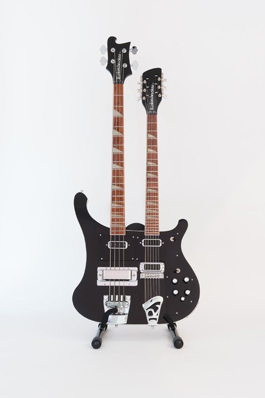 A double neck guitar is sitting on a stand on a white background.