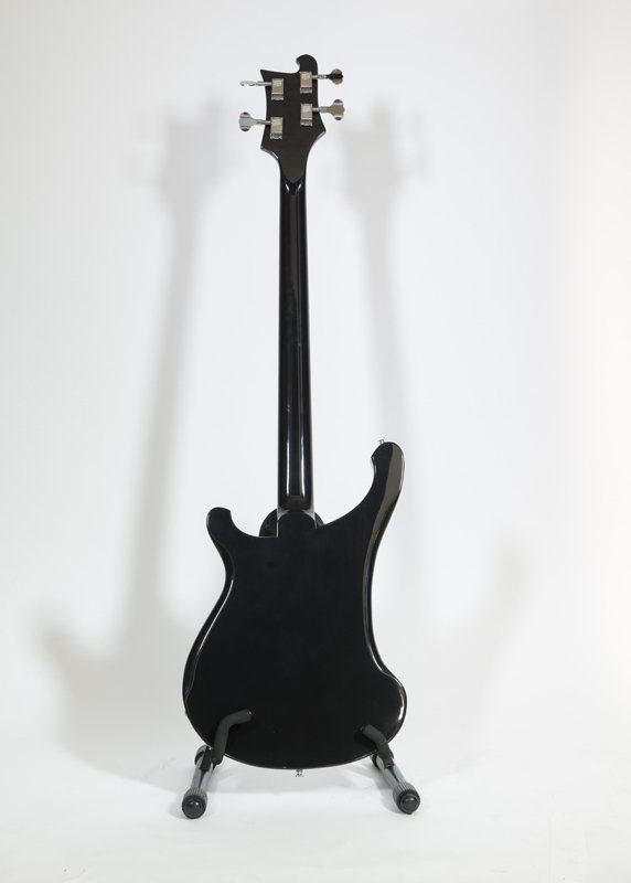 A black bass guitar is sitting on a stand on a white background.