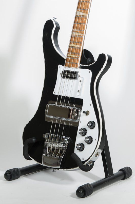 A black electric bass guitar is sitting on a stand