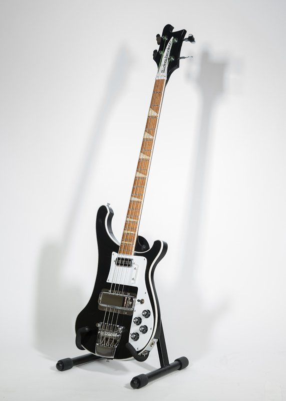 A black and white electric bass guitar is sitting on a stand.