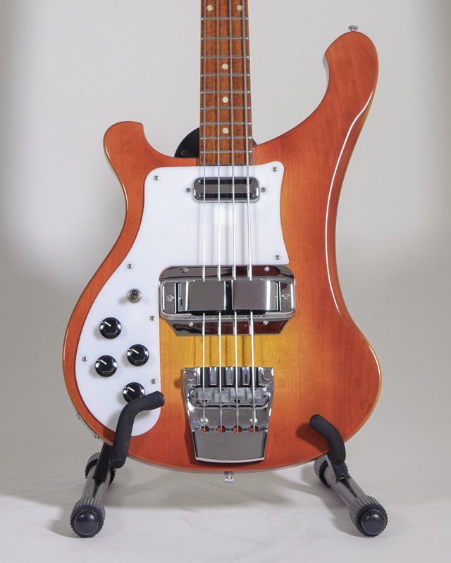 An orange and white bass guitar is sitting on a stand