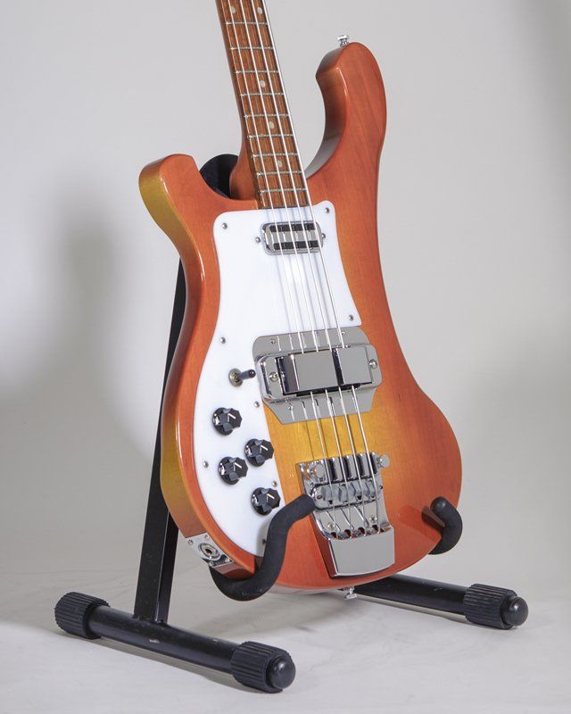 An orange and white bass guitar is sitting on a stand