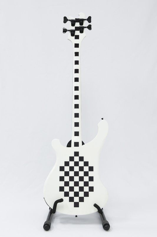 A white guitar with black squares on it is on a stand