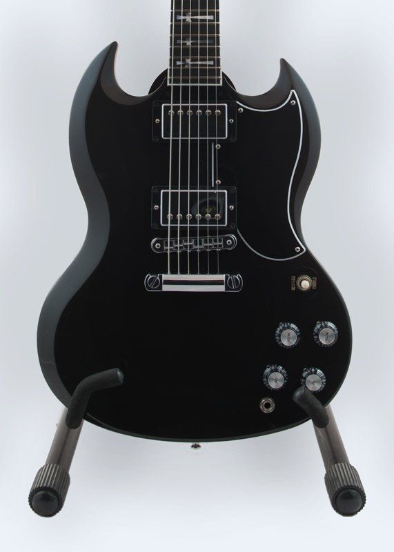 A black electric guitar is sitting on a stand