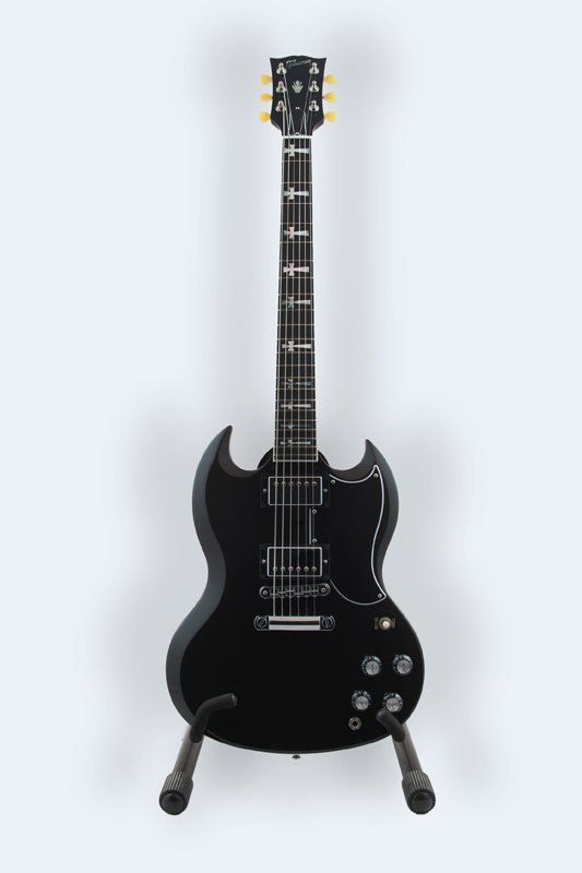 A black electric guitar is sitting on a stand on a white background.