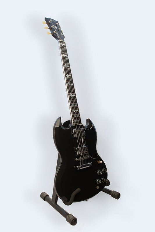 A black electric guitar is sitting on a stand.