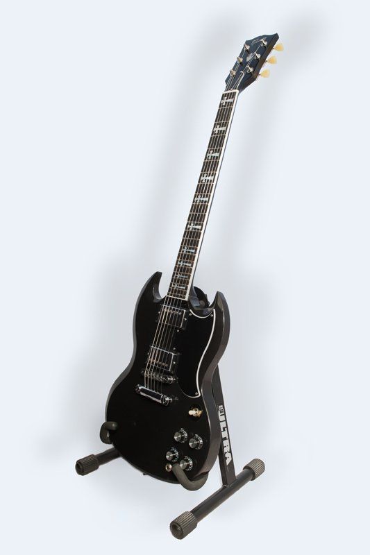 A black electric guitar is sitting on a stand.
