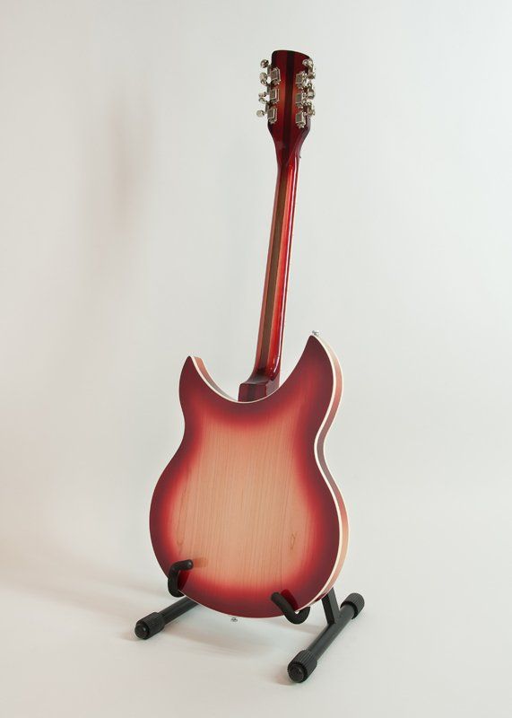 A red guitar is sitting on a stand on a white surface.