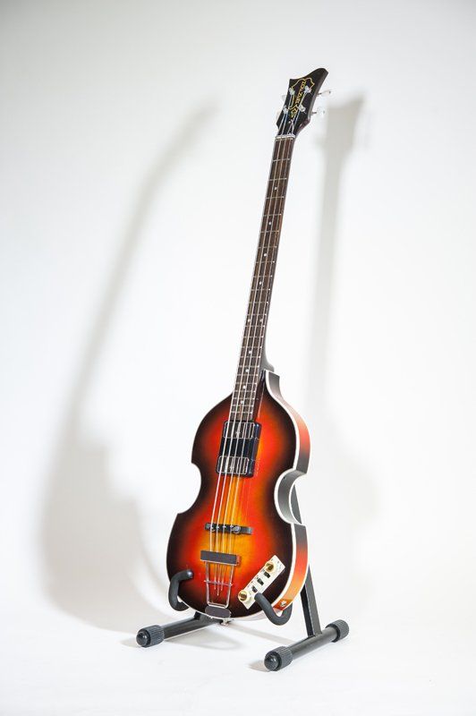 A bass guitar is sitting on a stand on a white background.