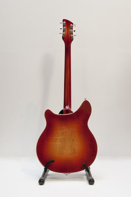 A red electric guitar is sitting on a stand on a white surface.