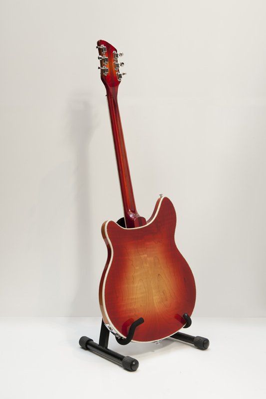 A red electric guitar is sitting on a stand.