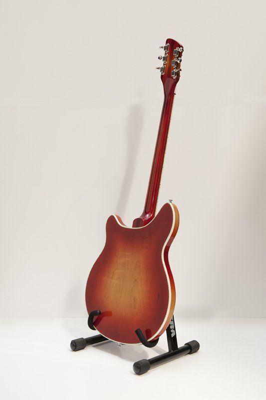 A red electric guitar is sitting on a stand.